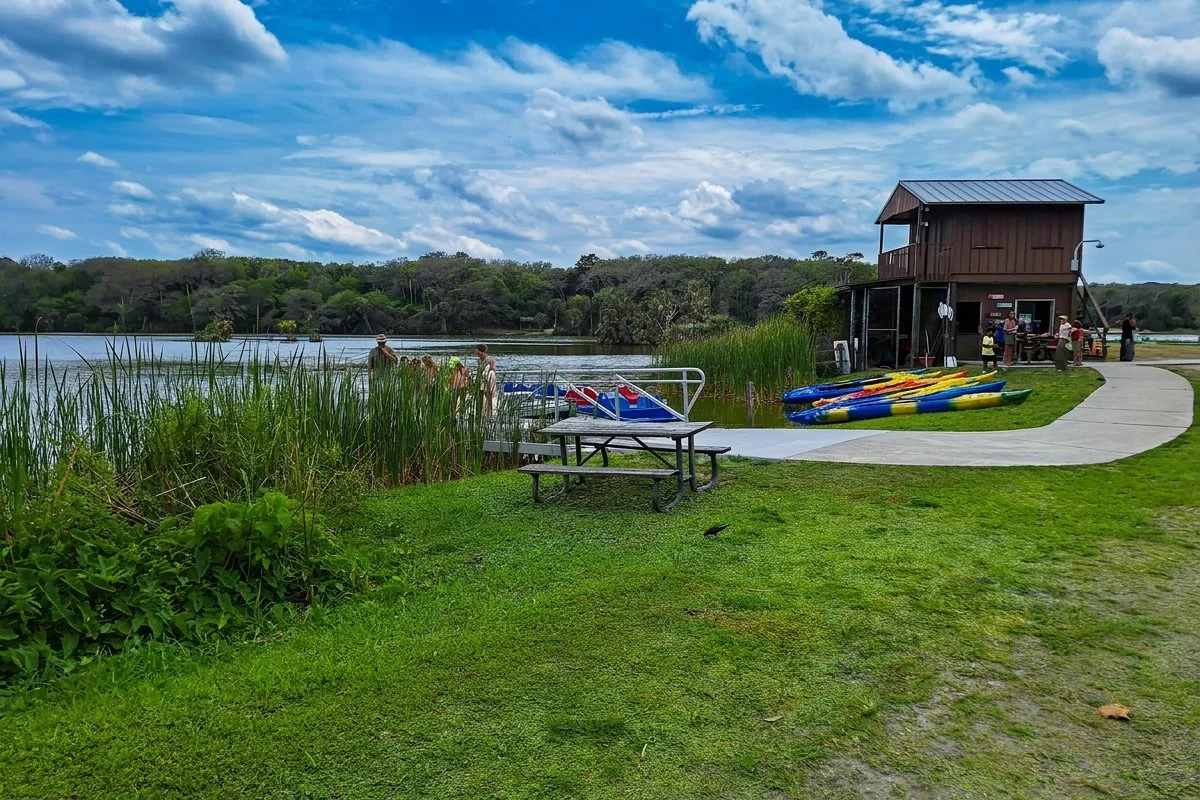 Kayak and paddleboat rental dock on Hanna Lake at Kathryn Abbey Hanna Park Jacksonville — colorful kayaks lined up beside the 60-acre freshwater lake with rental shop in background