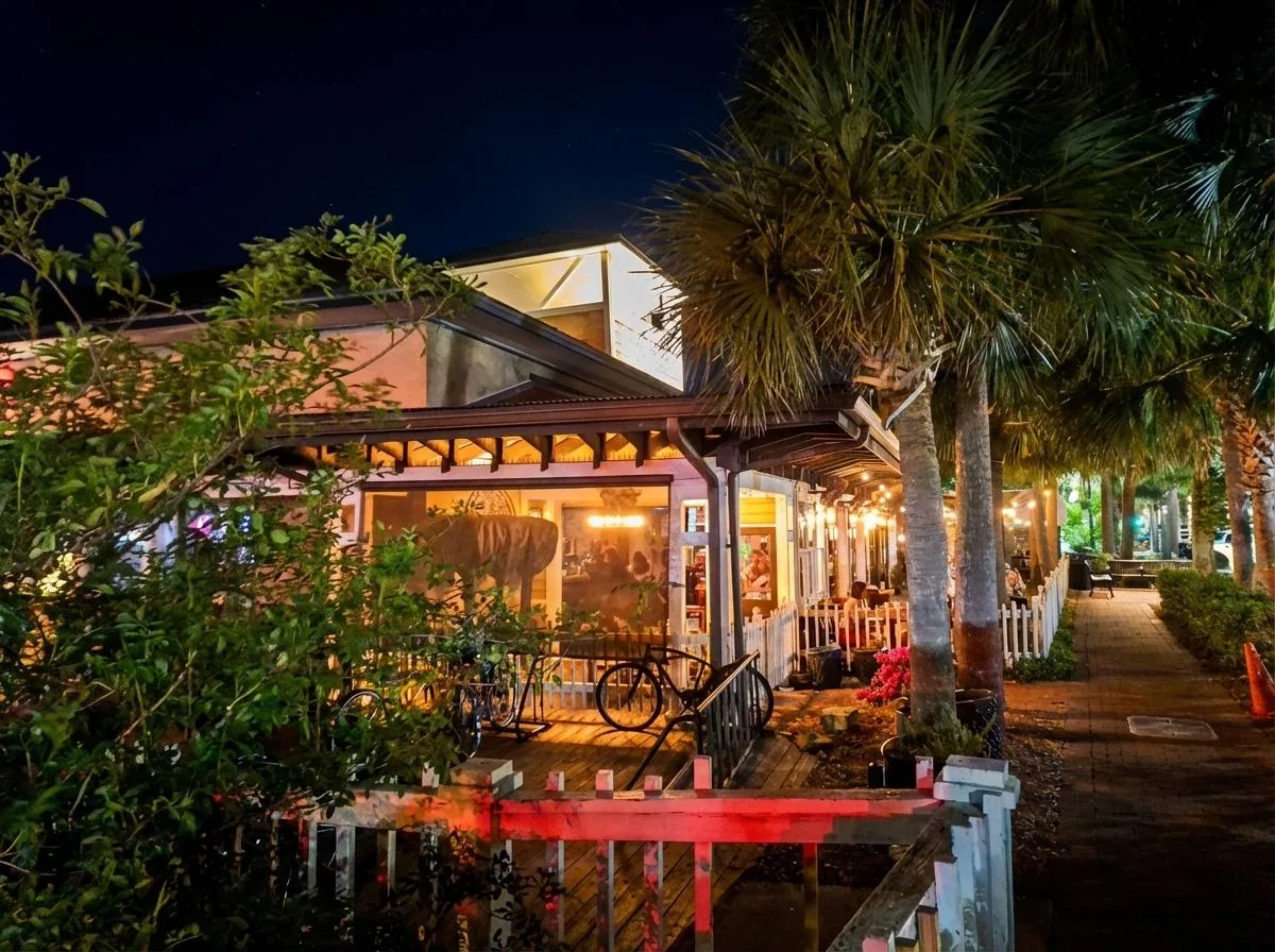 Poe's Tavern exterior at night with warm lights, bicycles, outdoor seating and palm trees in Atlantic Beach Florida
